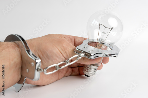 A man in handcuffs is connected to an electric light bulb. The concept of energy dependence.