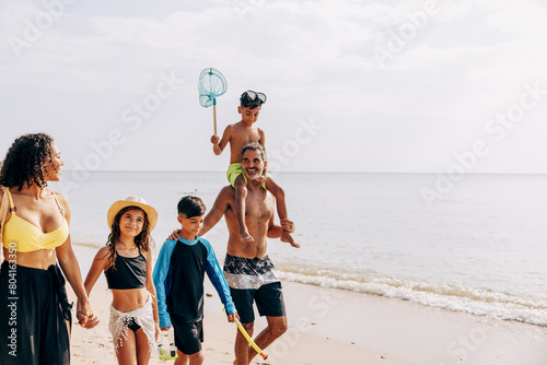 Father carrying son on shoulders while walking with family at beach against sky photo