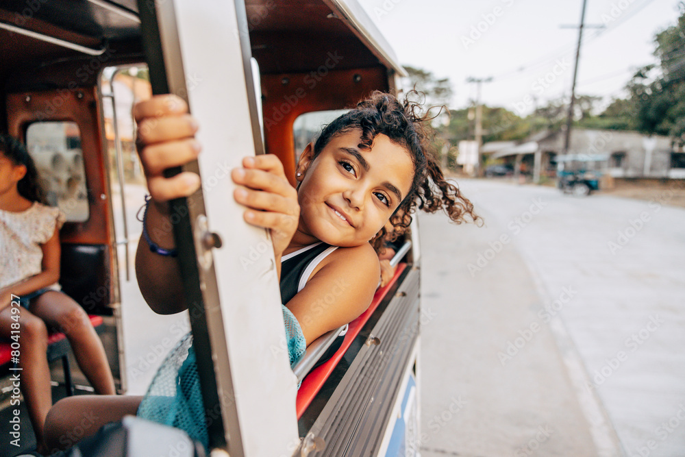 Smiling girl leaning out of window during road trip while sitting in tuk-tuk on vacation Smiling girl leaning out of window during road trip while sitting in tuk-tuk on vacation