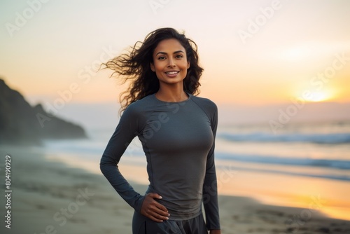 Portrait of a blissful indian woman in her 20s wearing a moisture-wicking running shirt over beautiful beach sunset