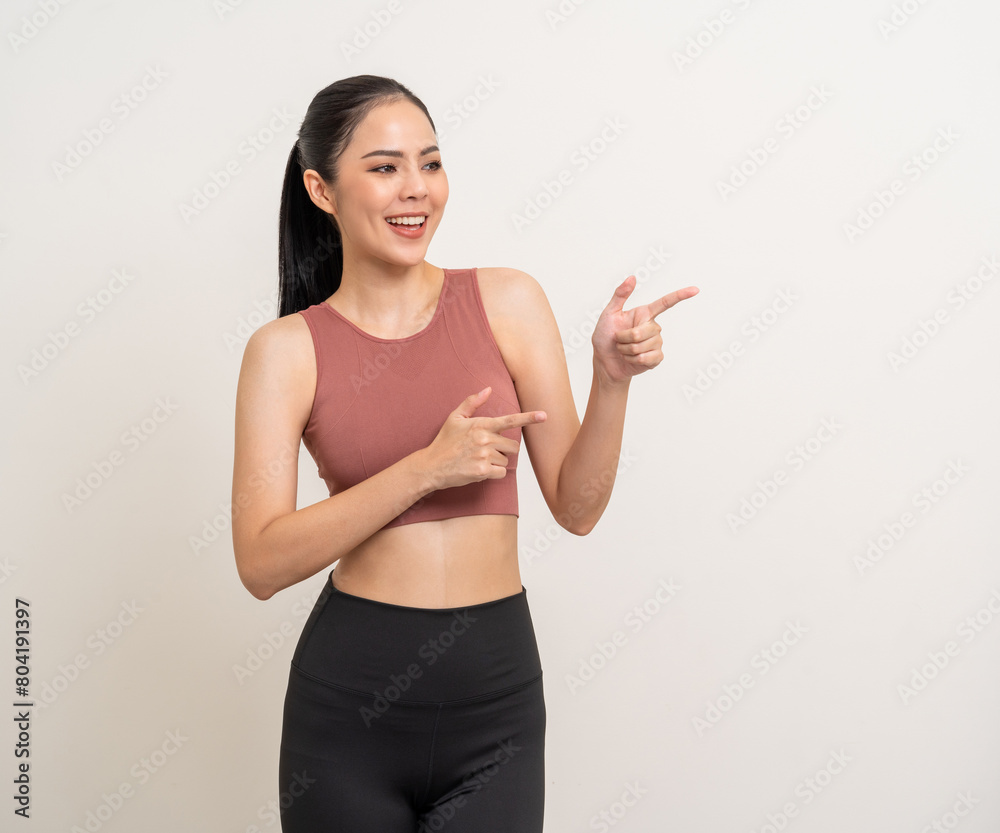 Young beautiful smiling asian woman with sportswear pointing finger to copy space on isolated. Happy healthy slim fit and firm latin attractive sporty woman standing pose exercise workout in studio. Young beautiful smiling asian woman with sportswear pointing finger to copy space on isolated. Happy healthy slim fit and firm latin attractive sporty woman standing pose exercise workout in studio.