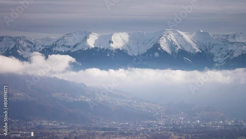 Snow-capped mountain range towers above the densely populated valley as clouds whirl below. Parallax video. photo