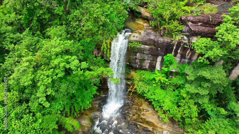 Aerial view of a lush tropical forest waterfall, captured by a drone, showcasing its breathtaking natural beauty. Soi Sawan Waterfall, Pha Taem National Park, Ubon Ratchathani Province, Thailand.
