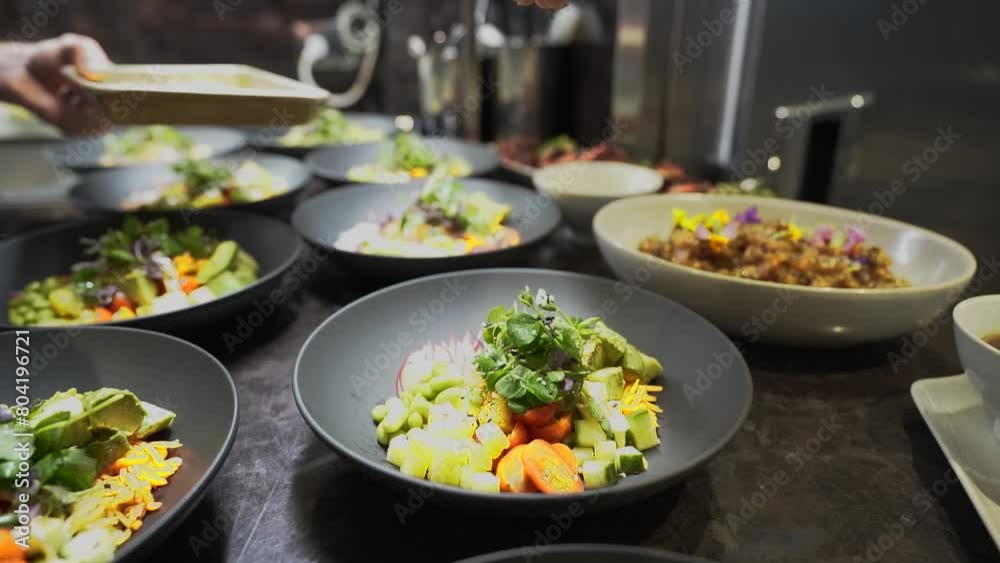 Hand sprinkles flaky salt on delicate fresh salad in prep kitchen, slow motion