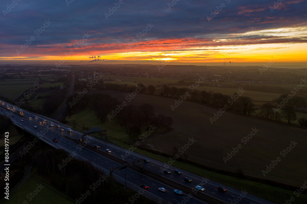 Aerial photo of the town of Garforth in Leeds UK overlooking the motorway at sunset with cars driving on the road while the sun sets in the background