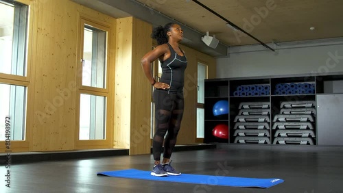 Standing in a split stance, one leg in front, and slowly moving forward in one bended knee on each side as the woman dips in lunges for her exercise. photo
