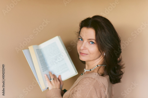 Studio portrait of beautiful 40 year old woman holding open old vintage book, posing on beige background
