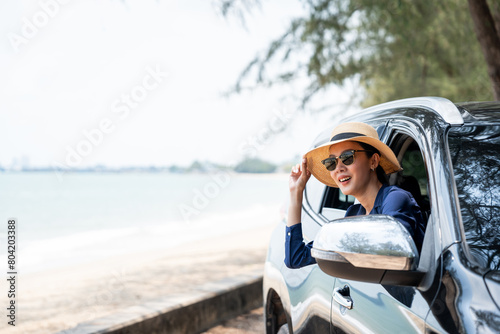 A young beautiful asian woman travel to the sea by car on a bright day. With beautiful blue sky. Vacation holiday weekend after hard work. Sticking her head outta the windshield