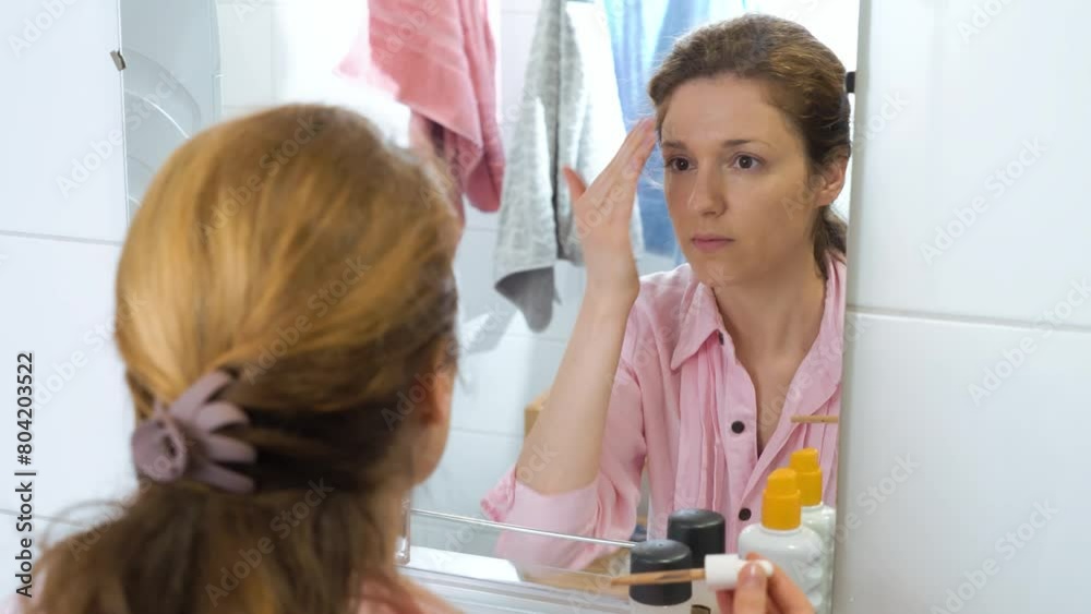 Beautiful caucasian middle aged woman uses foundation, concealer, and a correcting pencil in the bathroom Beautiful caucasian middle aged woman uses foundation, concealer, and a correcting pencil in the bathroom