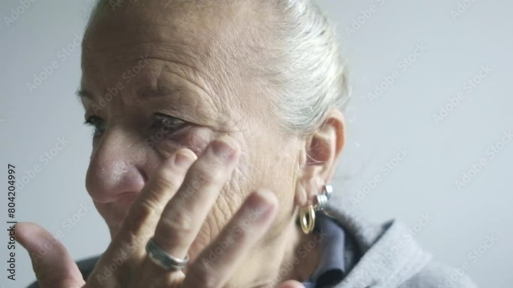 slow motion portrait elder senior woman  applies herself white cream make up wrinkles ageing concept