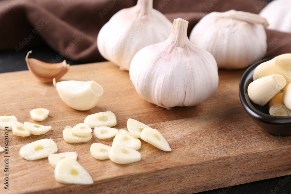 Aromatic cut garlic, cloves and bulbs on wooden board, closeup Aromatic cut garlic, cloves and bulbs on wooden board, closeup