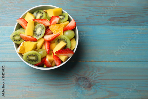 Tasty fruit salad in bowl on light blue wooden table, top view. Space for text