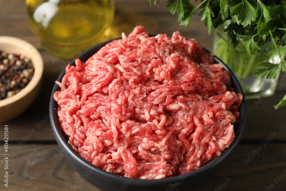 Raw ground meat in bowl and parsley on wooden table, closeup Raw ground meat in bowl and parsley on wooden table, closeup