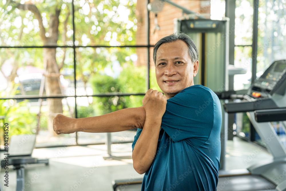 Senior asian man wearing sportswear warming up in fitness gym before exercise. Mature man stretching arm before running. Training athlete work out Senior asian man wearing sportswear warming up in fitness gym before exercise. Mature man stretching arm before running. Training athlete work out