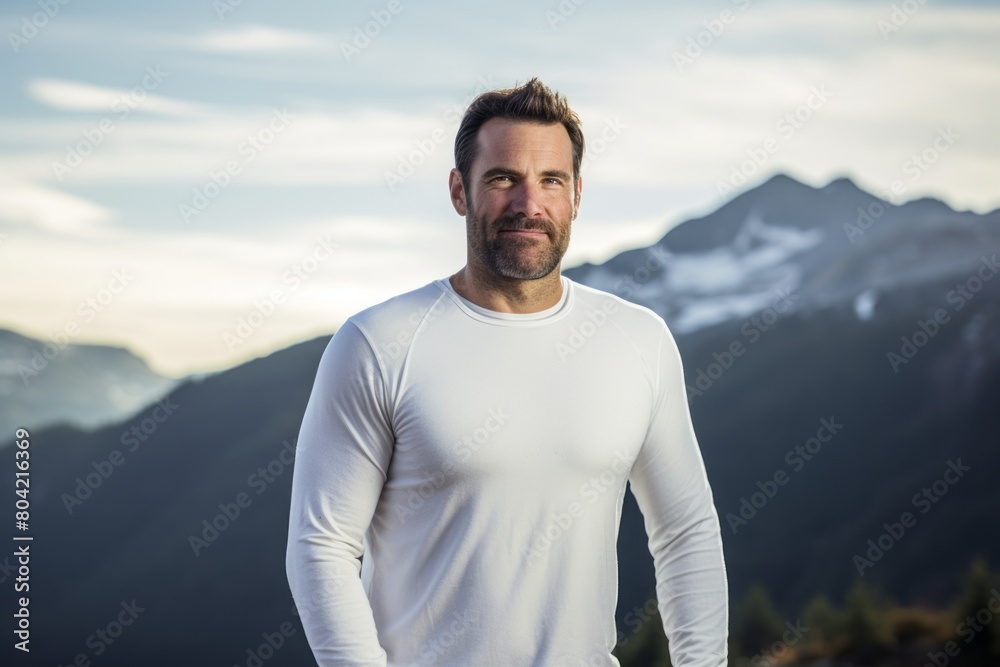 Portrait of a blissful man in his 40s sporting a long-sleeved thermal undershirt in backdrop of mountain peaks