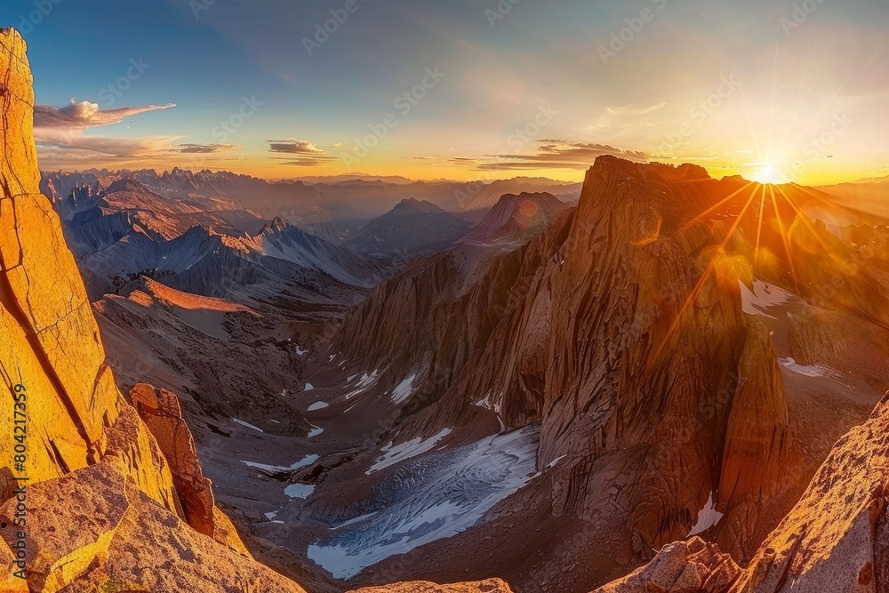 The sun sets over a vast mountain range, casting a warm golden glow on the peaks and valleys