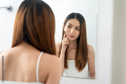 Self confident women look in the mirror brush up their hair and admire their body. Young asian beautiful woman who takes care of herself well. Check facial skin