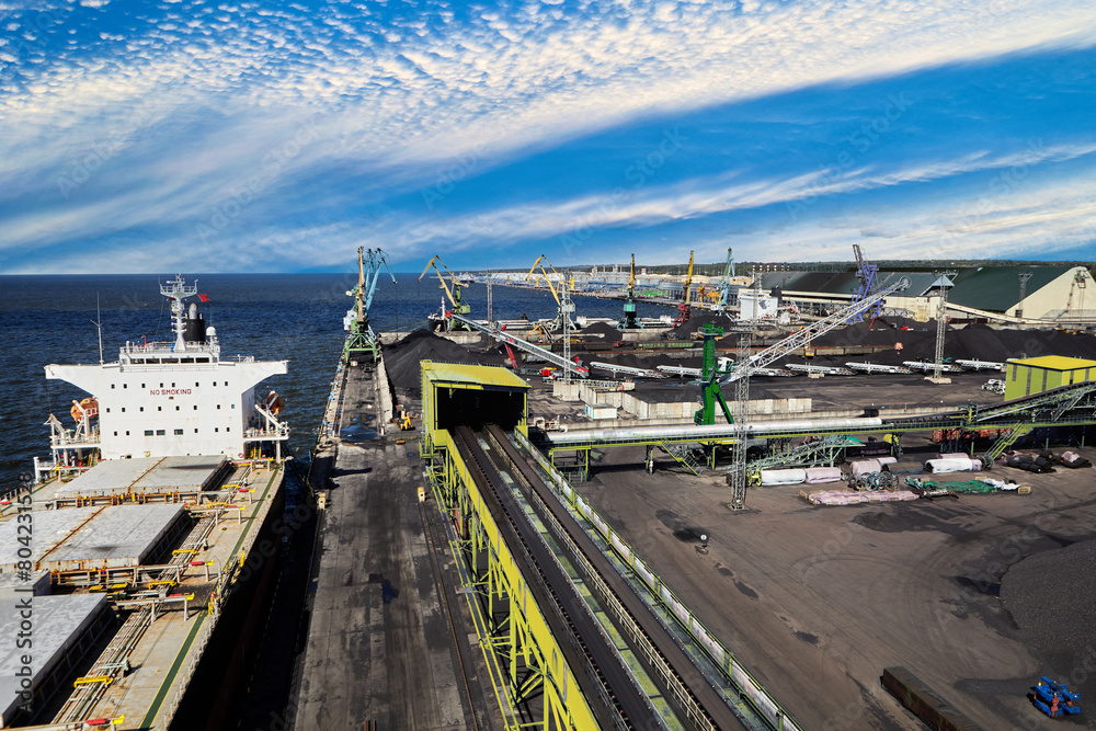 Coal Harbor and maritime bulk terminal with port cranes, coal embankments, bulk carriers at berth. Coal Harbor and maritime bulk terminal with port cranes, coal embankments, bulk carriers at berth.