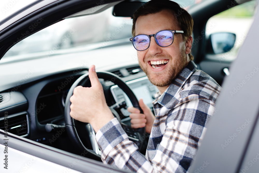 Man customer sitting in car salon and higgind the steering wheel, choosing auto and wanting to buy new automobile in showroom dealership store. Car sales concept Man customer sitting in car salon and higgind the steering wheel, choosing auto and wanting to buy new automobile in showroom dealership store. Car sales concept