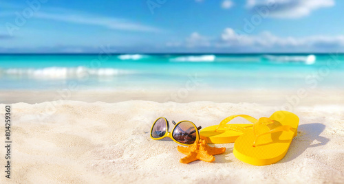 Summer beach background. Beach accessories - sunglasses, starfish, yellow flip-flops on sandy tropical beach against blue sky on bright sunny day.