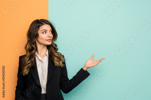 Confident businesswoman in a suit gestures with an open hand against a split orange and teal background, suggesting a presentation or the introduction of an idea or product
