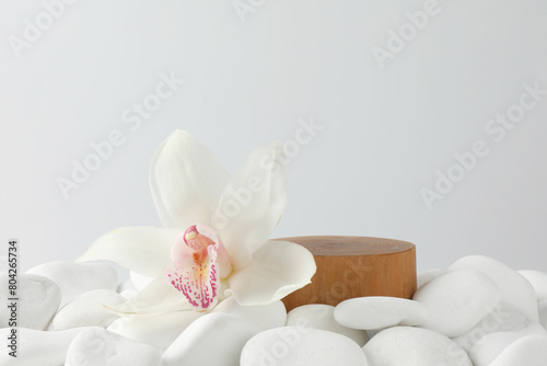 Presentation for product. Wooden podium and orchid flower on white pebbles. Space for text