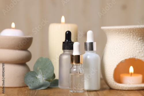 Different aromatherapy products  burning candles and eucalyptus leaves on wooden table  closeup
