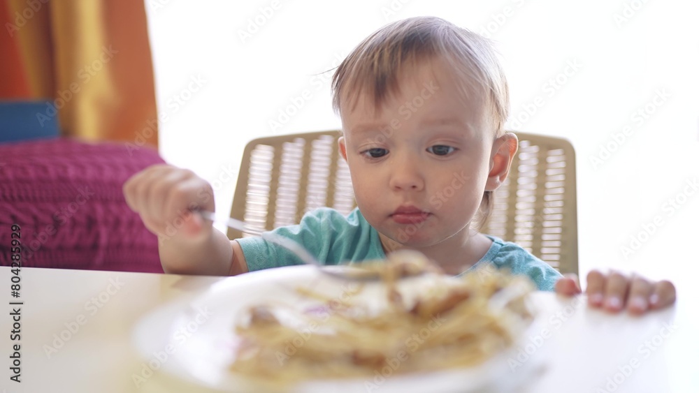 boy eating food at the table. happy family child dream concept. a little boy sits at the table and eats food with a spoon, against the backdrop of a large window food. child's lifestyle