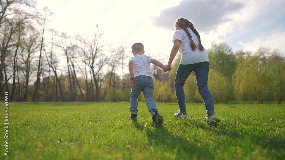 children running across the field. happy family child dream concept. a boy and a girl are running across a green field against the backdrop of a spring forest. child's lifestyle sporty children running across the field. happy family child dream concept. a boy and a girl are running across a green field against the backdrop of a spring forest. child's lifestyle sporty