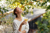 Relaxing with a Glass of Refreshing Kombucha, Surrounded by Nature's Beauty Happy woman enjoys a moment of detox and wellbeing in the sunlight, holding a glass of antioxidantrich kombucha infused with