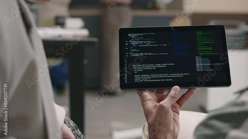 Closeup of two unrecognizable office program developers looking at digital tablet with codes running on black screen and having discussion
