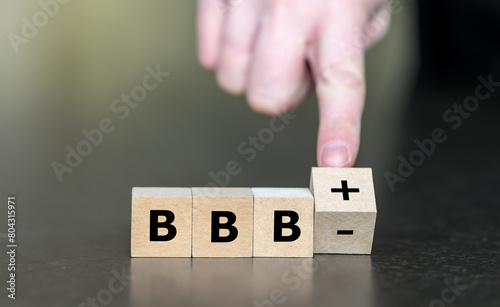 Hand turns wooden cube and changes the expression BBBminus to BBBplusplus. Symbol for a upgrade in a financial rating.