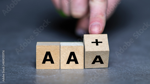 Hand turns wooden cube and changes the expression AAA to AAplus. Symbol for a downgrade in a financial rating.