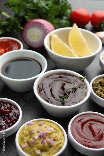 Different tasty sauces in bowls and ingredients on grey table, closeup