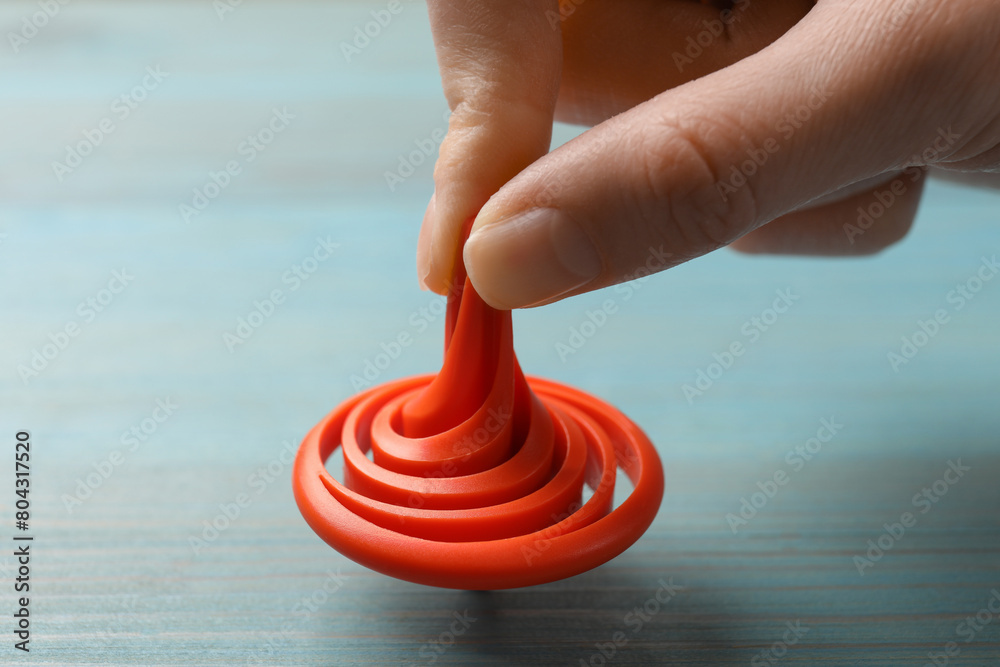 Woman playing with red spinning top at light blue wooden table, closeup Woman playing with red spinning top at light blue wooden table, closeup