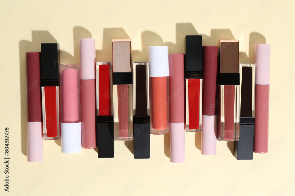 Fototapeta premium Different lip glosses on pale yellow background, flat lay