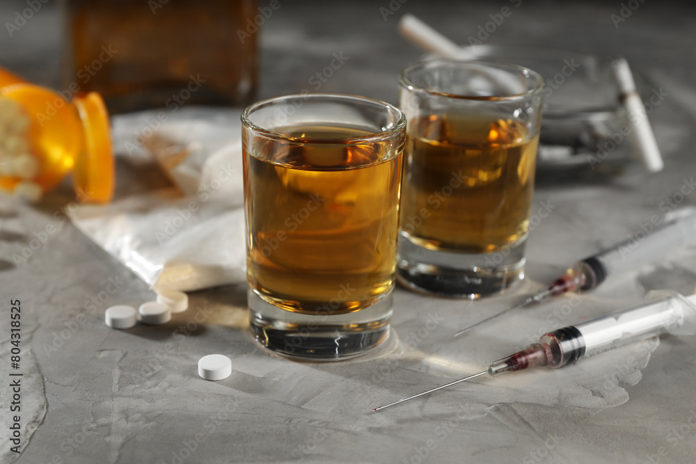 Alcohol and drug addiction. Whiskey in glasses, syringes, pills and cocaine on grey table, closeup Alcohol and drug addiction. Whiskey in glasses, syringes, pills and cocaine on grey table, closeup