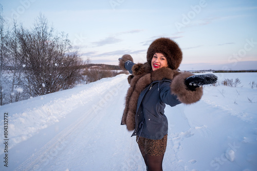 a beautiful girl in a fur jacket and hat walks and has fun in the winter forest.