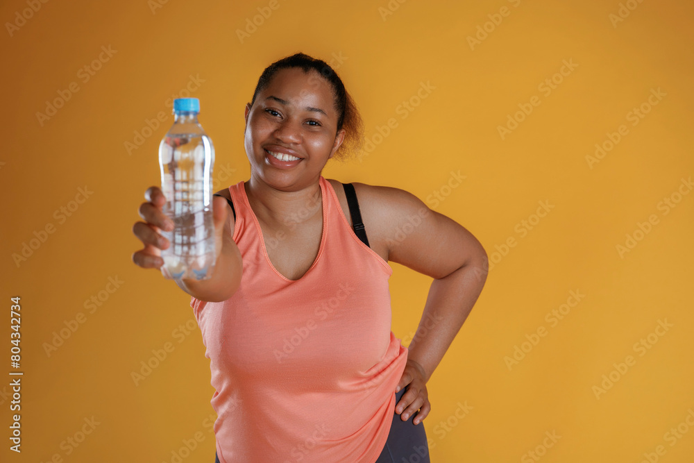 Showing bottle of water. African American woman is in the studio against yellow background Showing bottle of water. African American woman is in the studio against yellow background