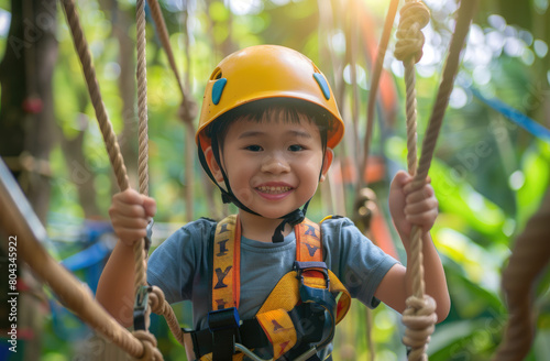 A happy child in safety gear and yellow gloves enjoying an adventure park, smiling while walking on the rope course with green trees as background