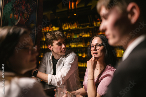 Positive young people enjoy communication and drinks in favourite pub. Young people locate near bar with bottles of elite drinks