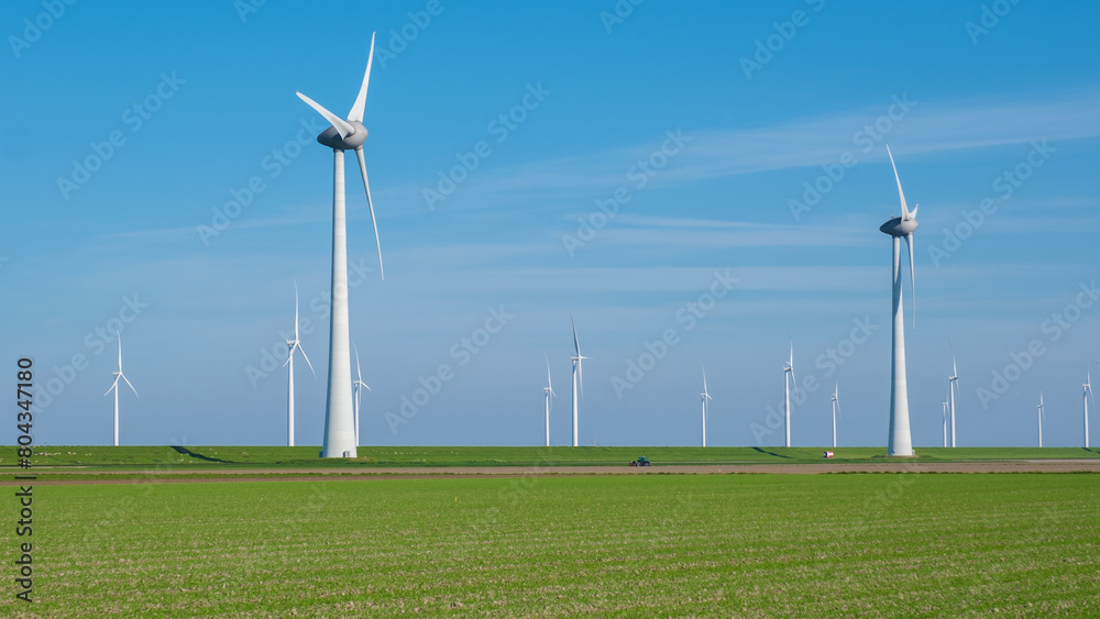 A vast field of lush green grass stretches out in the foreground, while a group of towering windmills spin gracefully in the distance against the clear sky of Flevoland, Netherlands A vast field of lush green grass stretches out in the foreground, while a group of towering windmills spin gracefully in the distance against the clear sky of Flevoland, Netherlands