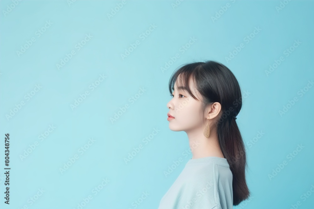 A woman with long brown hair and gold earrings stands in front of a blue wall A woman with long brown hair and gold earrings stands in front of a blue wall