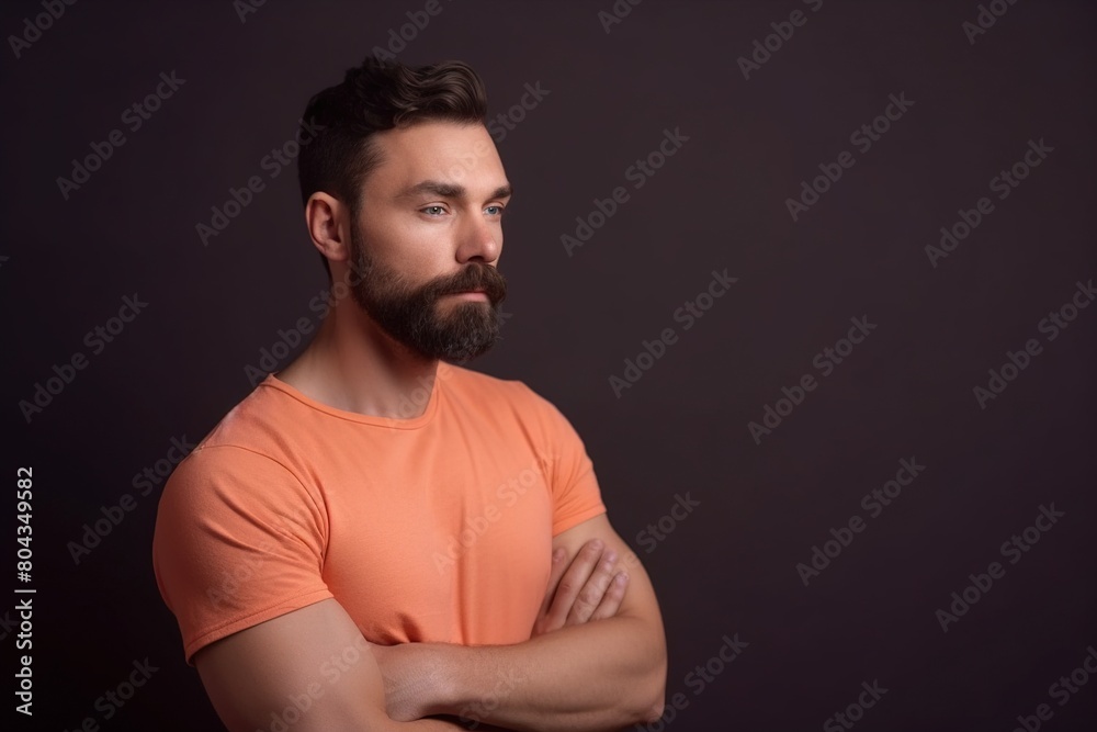 A man with a beard and orange shirt is standing in front of a dark background