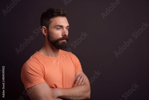 A man with a beard and orange shirt is standing in front of a dark background © Juan Hernandez