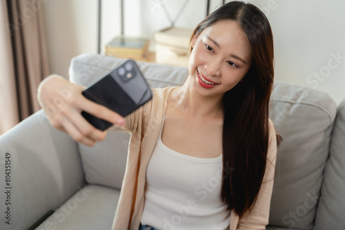 A woman is sitting on a couch and taking a selfie with her cell phone