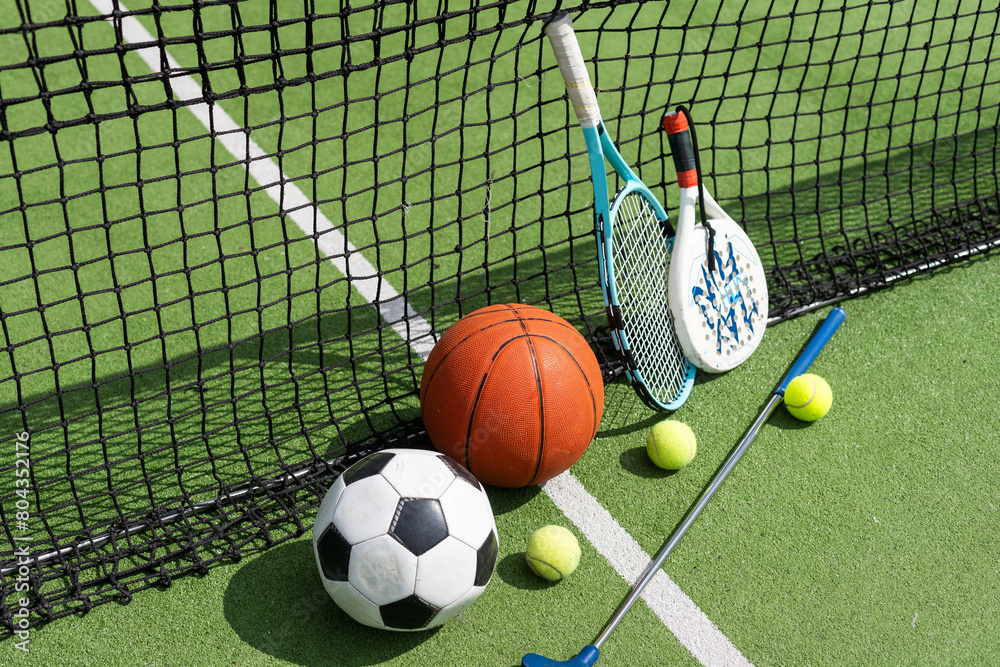 Fototapeta premium football soccer ball basketball tennis ball and racket laid on grass at sunset