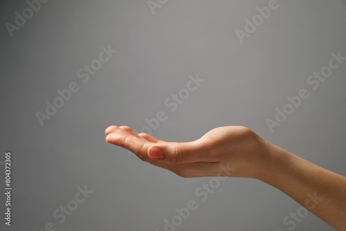 Woman holding something in hand on grey background, closeup. Space for text