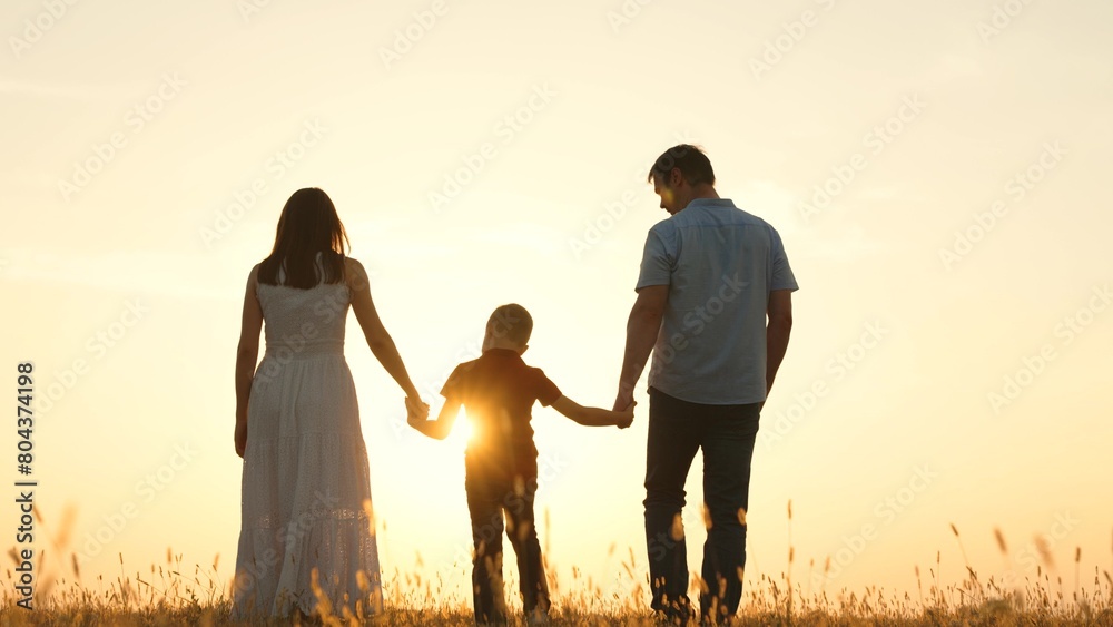 Family holding hands in field at sunset. Father dad kid boy child mother mom on golden rays sun go forward symbolizing hope bright future happy cheery memories time together. Strong family ties bonds