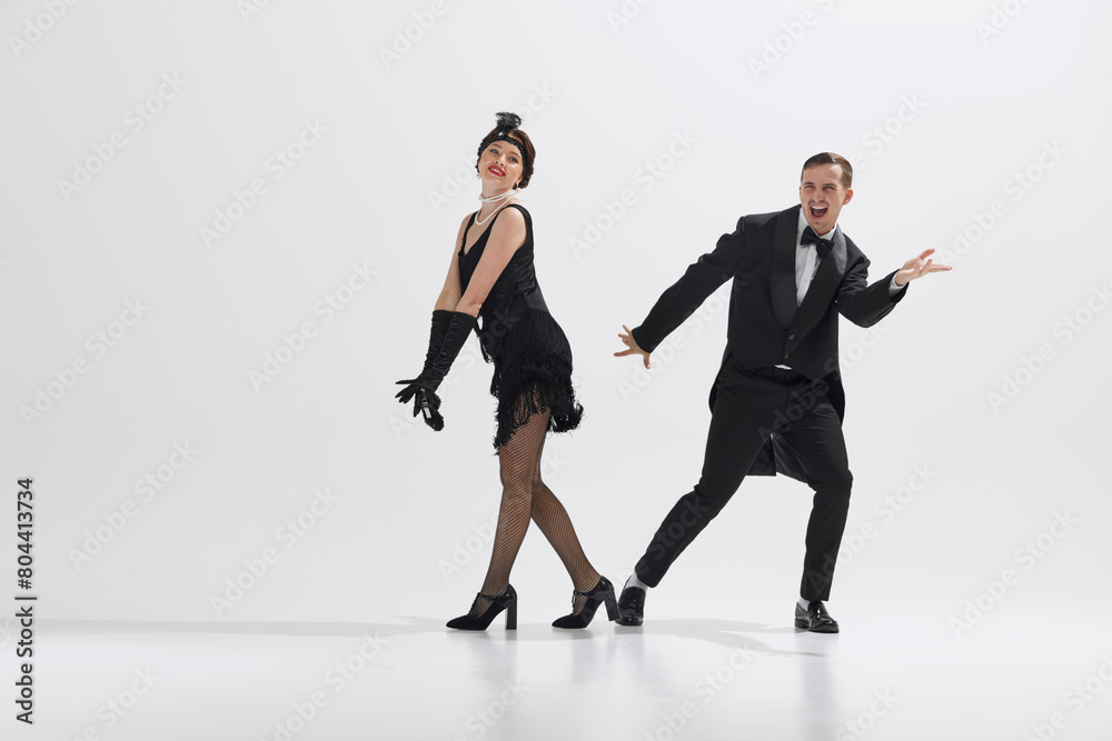 Fototapeta premium Joyful depiction of 1920s dance culture, young couple dressed in period costumes performing with enthusiasm isolated over white studio background. Concept of art, retro and vintage, entertainment, 20s